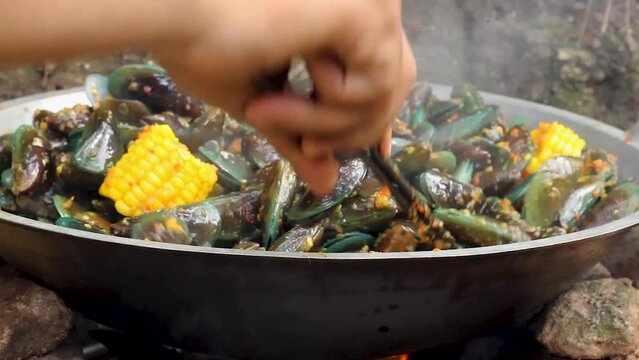 the process of cooking green mussels or Perna viridis, mixed with corn and spicy stir-fry spices.