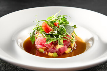 Tuna and avocado tartare topped with microgreens and cherry tomatoes, served in a white bowl