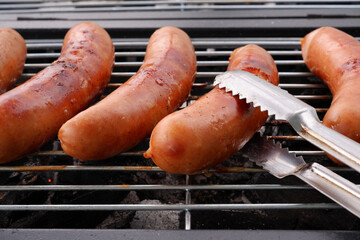 Flipping grilled sausages with metal tongues. Chef preparing  food for summer party.