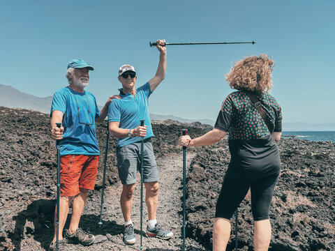 Outdoor activity in nature concept. Happy group of sporty mature friends enjoying healthy lifestyle hiking along a rocky beach in southern Tenerife enjoying nature and travel - Powered by Adobe