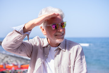 Portrait of bearded senior retired man outdoors at the seaside beach enjoying free time and relaxed vacation in a sunny day. Horizon over water