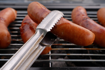 Metallic tongues holding grilled sausage in front of grill with sausages.