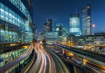 Fototapeta premium A view over the highway, in front of which there is an office building with glass walls and tall skyscrapers with lights on inside