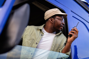 Truck driver using radio communication to park long vehicle in reverse at truck stop.