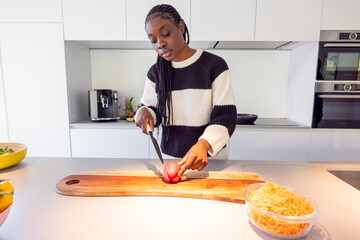 In a kitchen, a woman is seen cutting a tomato on a wooden cutting board. The setting suggests food...