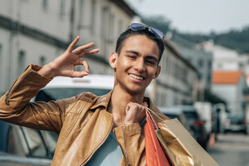young man with happy shopping bags on the street making ok sign