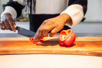 In the image, an individual is slicing a red pepper on a wooden cutting board. The scene involves...
