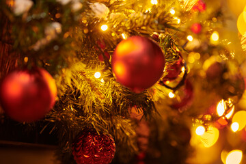 New Year christmas tree decorated Christmas balls with yellow flickering lights of garlands on green tree at night, merry Christmas and happy New Year mood with twinkling lights