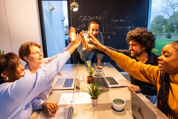 In a conference room, a group of people are enthusiastically giving each other high fives to share...