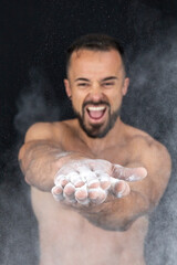 Strong shirtless man patting flour into his hands creating explosion