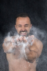 Strong shirtless man patting flour into his hands creating explosion
