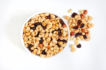 Peanut and raisin mix in round white bowl, isolated on white with loose bits around the bowl, with copy space