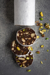chocolate sausage with cookies and pistachios on a gray background, wrapped in white paper