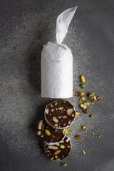chocolate sausage with cookies and pistachios on a gray background, wrapped in white paper