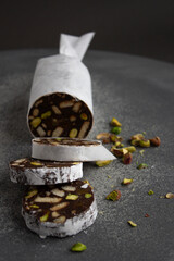 chocolate sausage with cookies and pistachios on a gray background, wrapped in white paper