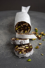 chocolate sausage with cookies and pistachios on a gray background, wrapped in white paper