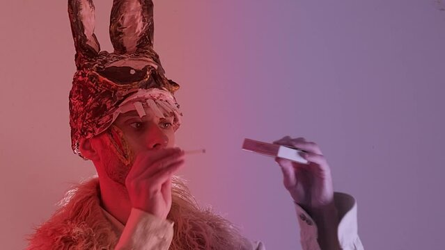 scary maniac man, young guy in cringe in scary bunny mask lights match, looks at fire, pyromania concept, theme of fear and horror, concept run while match burns, Halloween and Festive Costumes