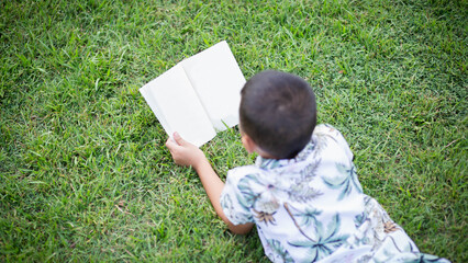 Little boy reading a book under big tree