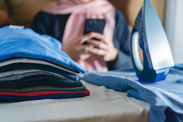 A stack of clothes that has been ironed, with a background of women with a headscarf playing with a...