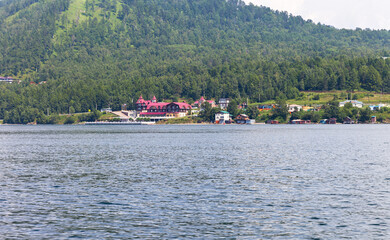 View from the water of the wooded shore of Baikal Lake and the village of Listvyanka in the distance. Summer trips on the lake by boat and outdoor recreation