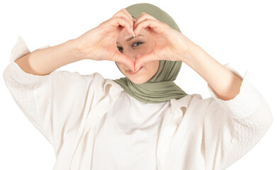Heart symbol, beautiful caucasian muslim girl in hijab demonstrate heart symbol with hands looking through. Selective focus on hands. Pretty young positive smiling islam religious woman lifestyle.