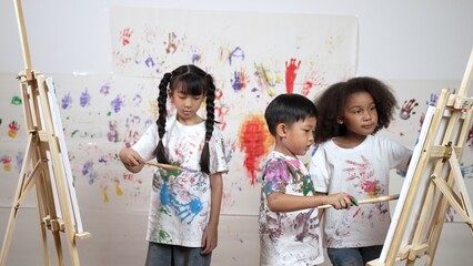 Diverse student painted or draw canvas at stained wall in art lesson. Asian girl wearing white...