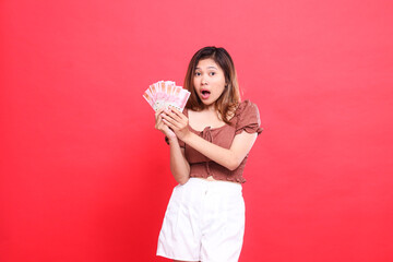 indonesia woman's expression shocked, both hands holding rupiah currency, wearing a brown blouse,...