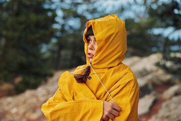 Young woman in a vibrant yellow raincoat admiring the scenic view of a rocky hill and lush trees on...