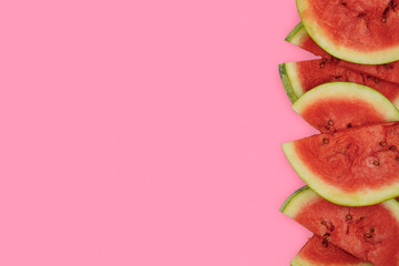 Summer fruit background concept, a side border of half slices of red juicy watermelon on pink...