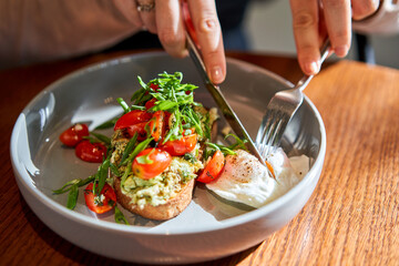 Open brioche sandwich with mint avocado, poached egg served with arugula and cherry tomato. Healthy...