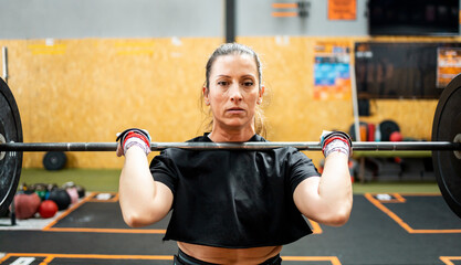 A middle-aged woman is weightlifting inside a large gym.The 50-year-old woman lifts the bar with...