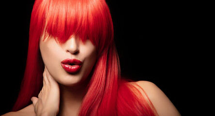 Beautiful model with long, healthy dyed red hair and bold lips posing against a black background