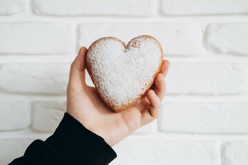 A heart-shaped donut sprinkled with powder in a man's hand close-up.