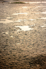 Shallow muddy puddle with a clear orange sky reflected on its surface. Lush green grass and a few blades of brown grass border the puddle.