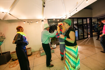 A group of friends is having a great time at a retro costume party, dancing on a rooftop under...