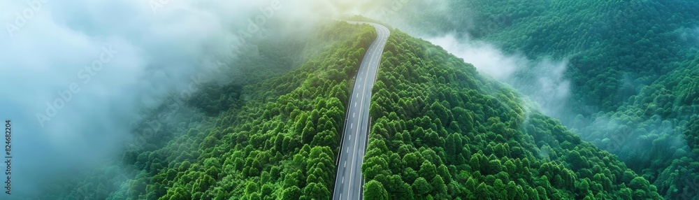 Aufkleber aerial view of a winding road through lush green forest with morning fog creating a serene and mysti