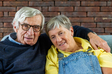 An elderly couple is relaxing on a sofa, displaying love and happiness in their cozy home...