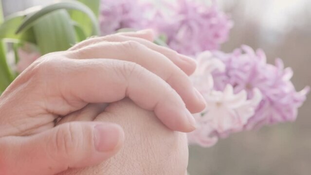 close-up hands elderly woman on pink hyacinth flowers background, Aging and beauty, graceful wrinkles, Empowerment and resilience, anti-aging cosmetology and care for aging skin, Health and wellness