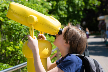 a boy looks through a yellow stationary field view binocular - binoscope, in the park.