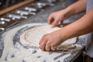Pizza dough being rolled and kneaded. Cook hands kneading dough, sprinkling piece of doughs with...