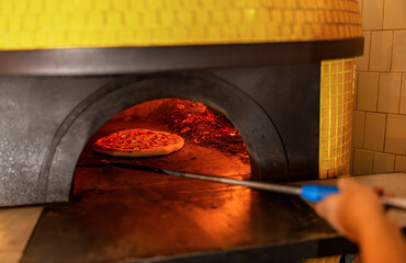 Pizzaiolo while checking a pizza being cooked in the wood oven with his oven shovel. Pizza concept....