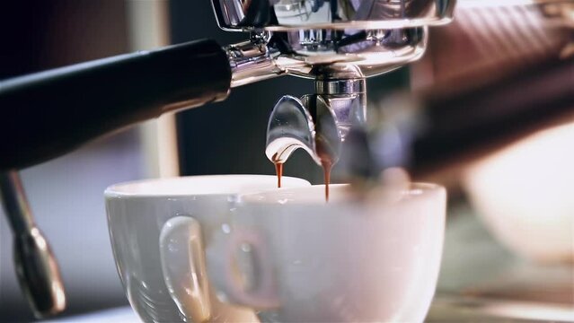 Close-up of the Espresso coffee extraction from a professional coffee machine with a bottomless filter. Coffee flowing into cup. Coffee aroma and the warm shop atmosphere