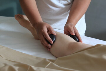 Close-up cut of professional masseuse doing hot stone massage service to her female customer, relaxation, spa treatment, wellness, resort, hotel, leisure.