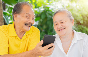 Happy Asian Elderly Couple laughing sitting on garden chair while using smarting technology in the garden.