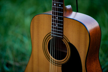 Acoustic guitar, orange string musical instrument placed in the area of trees and grass, playing...