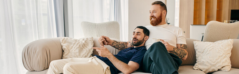 A gay couple in casual clothes sitting on a couch in a modern living room.