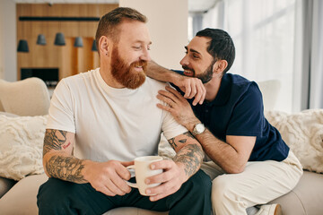 A gay couple in casual attire relax on a couch, enjoying each others company and sipping coffee in...