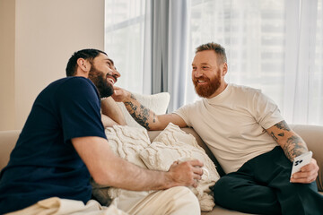 Two happy gay men in casual clothes engaged in a deep conversation while sitting on a modern couch...