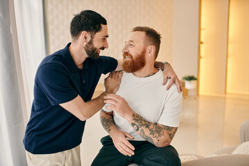 Two men in casual clothes hug each other warmly in a modern living room, showing affection and love...