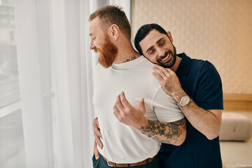 Two men in casual clothes embracing in front of a window, showcasing love and connection in a...